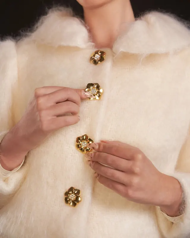 Detalle de botones joya con forma de flor dorada sobre chaqueta de mohair marfil